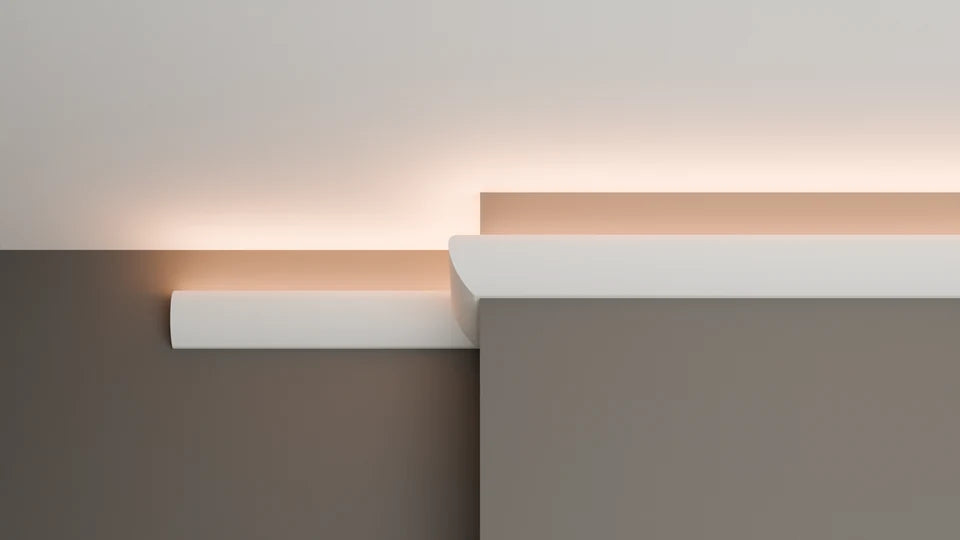 A modern wall-mounted linear light fixture in a minimalist interior setting, casting a warm peach glow against a neutral beige and taupe background.